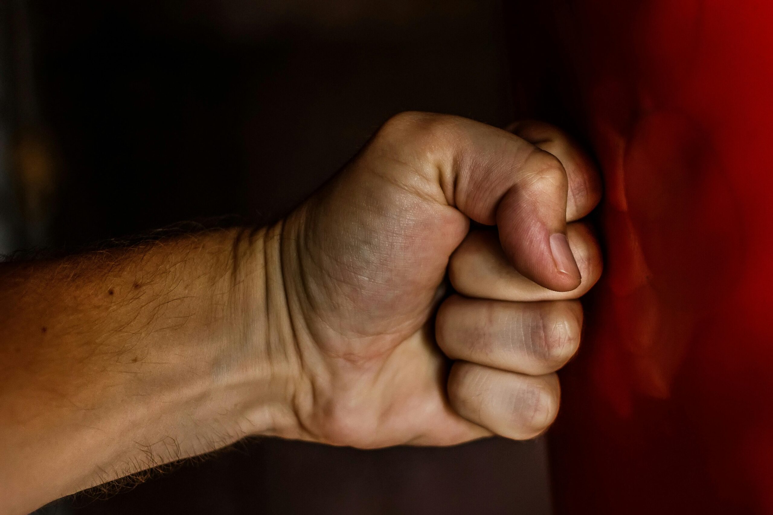 A close-up of a clenched fist striking a red punching bag, showing tension and impact as the hand meets the surface.