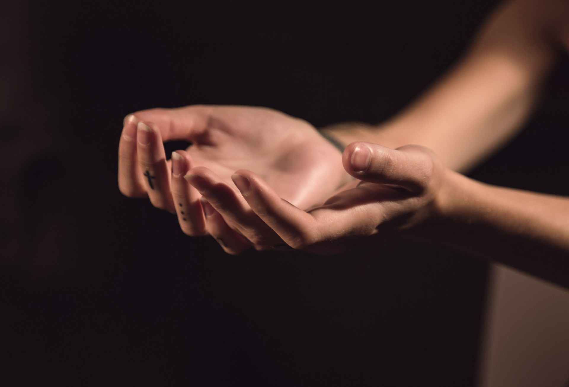 A close-up of open hands held gently in front of a dark background, palms facing upward in a gesture of openness and receptivity.
