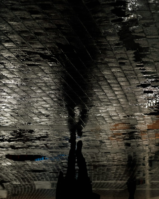 A dark figure reflected in wet paving stones
