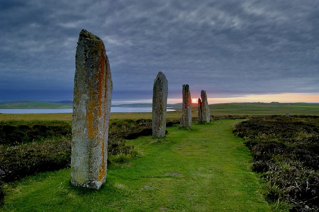 Standing stones aligned across a grassy landscape beneath a cloudy sky.